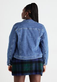 Τζάκετ από τζιν με σκούρο μπλε ξεβάμμα, διαθέτει κλασικό γιακά, μακριά μανίκια και λεπτομέρειες ραψίματος. Συνδυάζεται με φούστα σε πράσινη καρό.