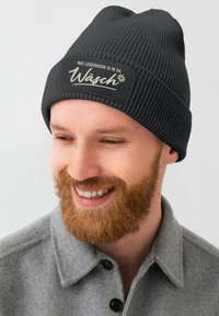Schwarze gestrickte Mütze mit geripptem Muster und einem rechteckigen Patch, der weißen Text und ein florales Motiv zeigt.