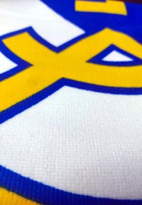 Tessuto giallo e blu con grande testo stilizzato su uno sfondo bianco, con una trama testurizzata e bordi netti.