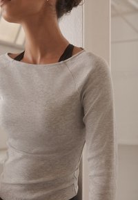 Graues, geripptes Langarmshirt mit weitem Ausschnitt und figurbetontem Schnitt. Das Oberteil verfügt über eine strukturierte Stoffoberfläche und sichtbare Nahtdetails.