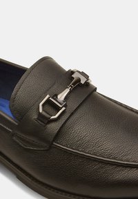 Schwarzer Lederloafer mit strukturiertem Finish, ausgestattet mit einem glänzenden metallischen Schnallen-Detail und einer blauen Innenauskleidung.