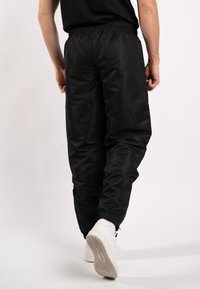 Zwarte nylon joggers met een elastische tailleband en enkels, met een zachte textuur en een losse pasvorm. Draag je met witte sneakers.