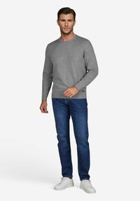 Grauer Strickpullover mit Rundhalsausschnitt, kombiniert mit dunkelblauen Jeans und weißen Turnschuhen. Das Model steht entspannt mit den Händen an den Seiten.