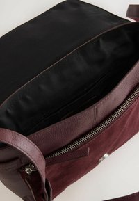 Borsa bordeaux con esterno in pelle liscia, pannello in suede testurizzato, zip in argento e interno foderato in tessuto nero.