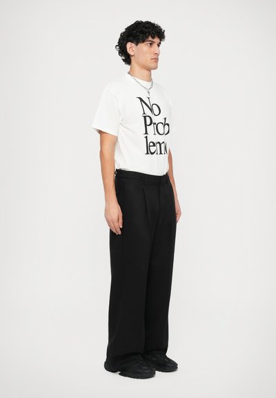Weißes Baumwoll-T-Shirt mit schwarzem Text "No Problem", kombiniert mit lockeren schwarzen Hosen und schwarzen Turnschuhen, mit einem lockeren Schnitt und glatter Textur.
