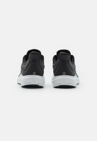 Un paio di scarpe sportive nere e grigie viste da dietro, con suole bianche e dettagli di logo sottili su uno sfondo bianco.