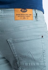 Shorts de mezclilla azul claro con un acabado texturizado, que cuentan con dos bolsillos traseros y una etiqueta rectangular de cuero marrón con detalles de marca.