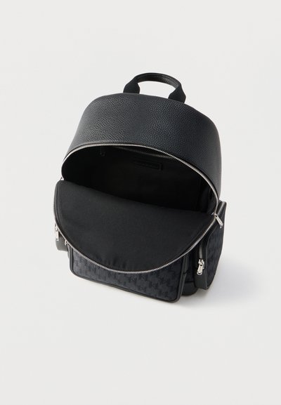 Sac à dos noir texturé avec compartiment principal ouvert, poche avant et poches latérales zippées sur fond blanc.