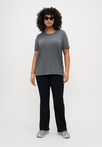 Gray short-sleeve t-shirt, relaxed fit, worn with black pants and gray sneakers. Model has curly hair and sunglasses.