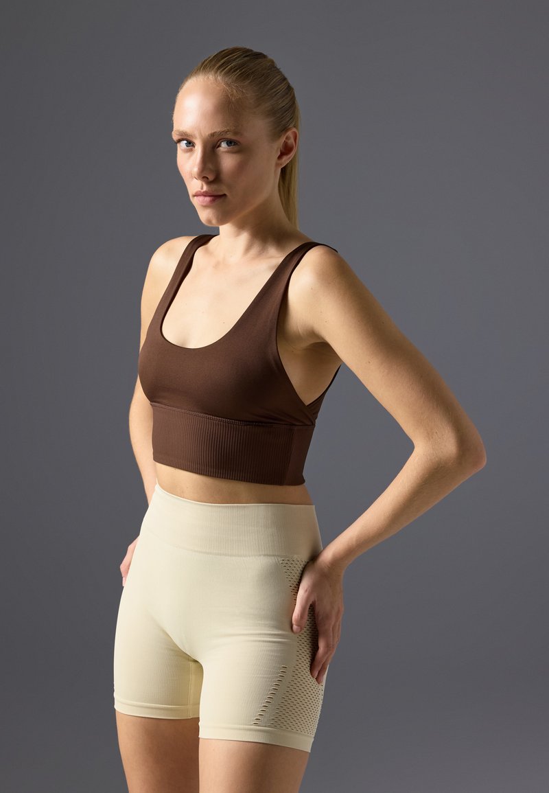 Top corto de rayas marrón combinado con pantalones cortos de ciclismo beige claro que tienen un panel texturizado. Ambas prendas son ajustadas y elásticas.