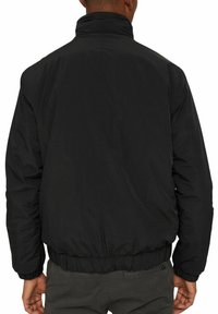 Giacca bomber nera, isolata, con colletto alto, polsini e orlo elasticizzati. Texture liscia e design minimalista, senza loghi o dettagli visibili.