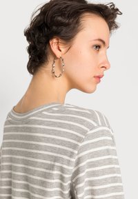 Top listrado cinza e branco com decote redondo, textura suave e mangas curtas, combinado com um brinco em forma de argola torcida de prata.