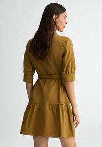 Robe jaune moutarde en tissu léger, dotée de manches courtes, d'une ceinture à la taille et d'une jupe à volants superposés.