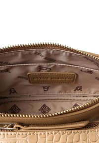 Interno di borsa beige con texture, dotato di cerniera dorata, un rivestimento morbido e un motivo ripetuto con il logo "Steve Madden".