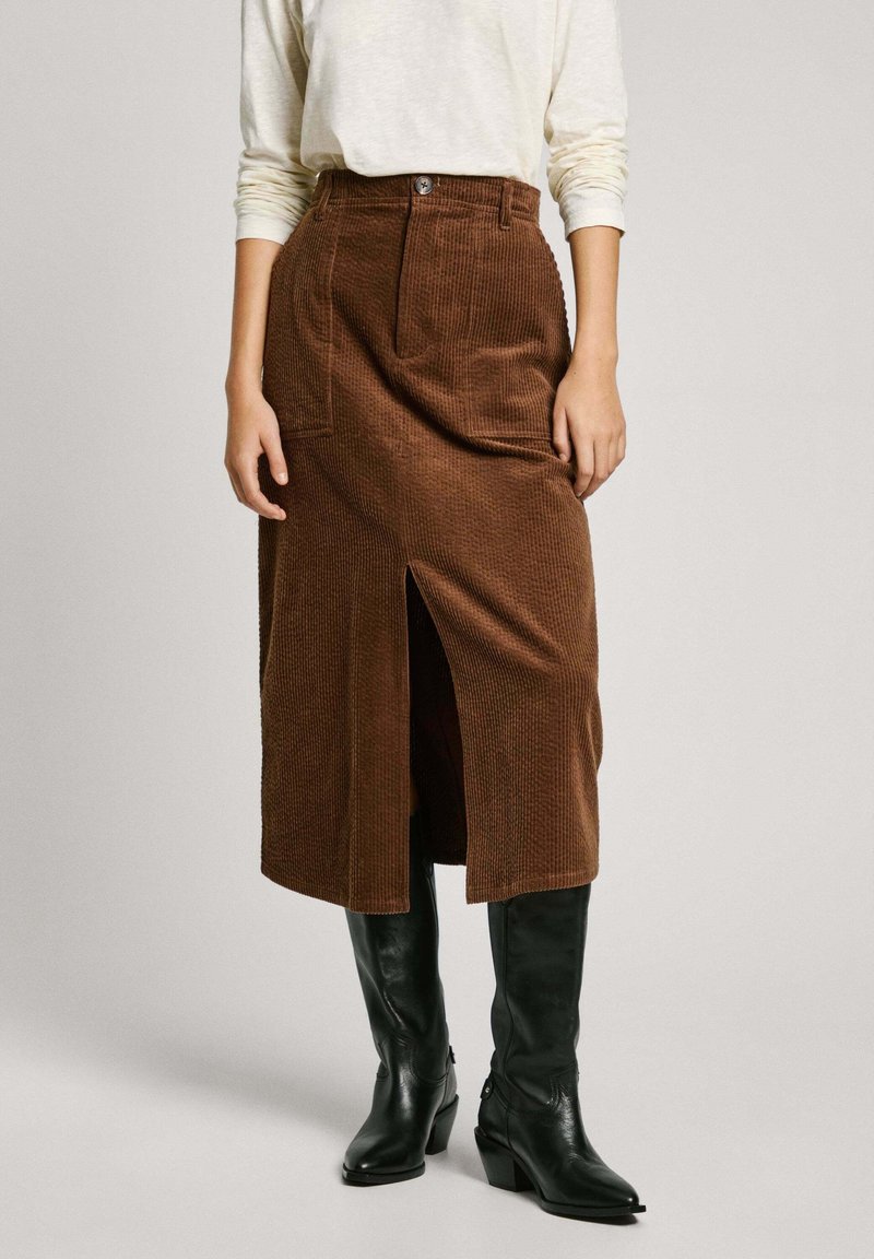 Gonna midi in corduroy marrone con spacco frontale, vita alta e tasche frontali, abbinata a stivali di pelle neri al ginocchio.