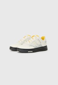 Sneakers met een bovenwerk van crème en grijs gaas, gele accenten, witte veters en een zwarte rubberen zool met een gestructureerd loopvlak.