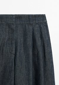 Dark blue denim pants showing waist with belt loops and front pleat details on a white background.