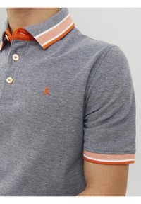 Polo gris à manches courtes avec col et bords de manches rayés orange et blanc, avec un petit logo orange brodé sur la poitrine.