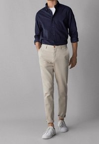 Marinblå skjorta med knappar, vit t-shirt under, beige chinos och vita sneakers. Slät tyg, slim fit, upplupna ärmar på skjortan.