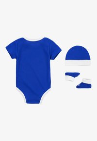 Kék pamut kezeslábas fehér díszítéssel, hozzá illő sapkával és cipőkével. Minden darab sima felületű és egyszerű dizájnú.