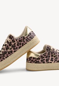 Paire de baskets compensées à imprimé léopard avec semelles tissées beiges et accents métalliques dorés au talon, présentées sur un fond blanc.