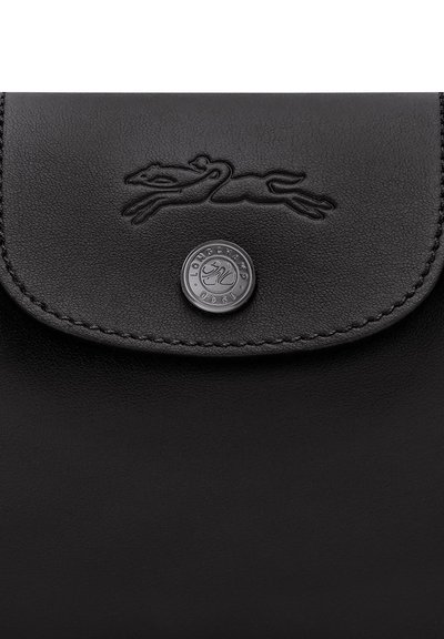 Black leather flap with embossed running greyhound logo and round metal button engraved with brand name and year.