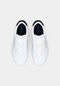Ein Paar weiße Tommy Hilfiger Sneakers mit weißen Schnürsenkeln und schwarzen Innensohlen, von oben auf einem hellen Hintergrund betrachtet.