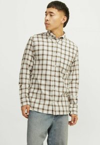 Camisa de botones de manga larga en beige con un patrón a cuadros marrón oscuro, con cuello y dobladillo recto, combinada con jeans de un azul claro.