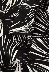 Camicia bianca e nera con un motivo a foglia, realizzata in tessuto dalla texture liscia. Include bottoni neri e un colletto.
