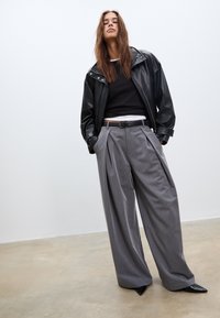 Crna kožna jakna, crni džemper i sivi plisirani hlače. Hlače imaju visok struk; crne cipele s oštrim vrhom upotpunjuju odijelo.