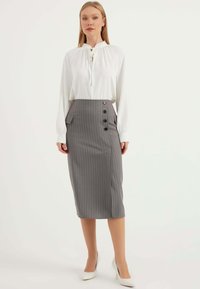 Weiße Bluse mit einer Halsband, kombiniert mit einem grauen, gestreiften Bleistiftrock mit seitlichen Taschen und vier schwarzen Knöpfen. Absatzschuhe runden den Look ab.