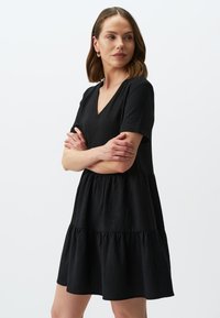 Zwart jurkje van gestructureerde stof, met een V-hals, korte mouwen en een gelaagde, uitlopende rokontwerp. Eenvoudige en veelzijdige stijl.