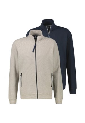 Kahden miehen vetoketjulliset takit, toinen beige edessä ja toinen tummansininen takana, molemmissa pystypaidat ja vetoketjulliset sivutaskut.