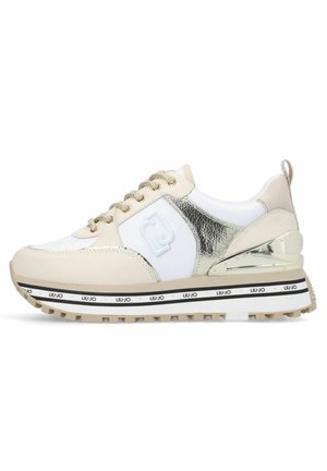 Beige ja valge sneaker, millel on läikiv kuldne aktsent, tekstureeritud materjalid, paks valge tald mustade ja kuldsete detailidega ning ümmargused paelad.