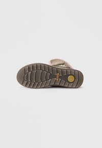 Semelle de chaussure en caoutchouc brun avec un motif de bande de roulement linéaire, présentant un logo de marque et des détails en relief. Textile rose pâle autour du bord supérieur.