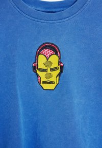 Blue cotton t-shirt featuring an embroidered Iron Man face in yellow, red, and black with textured details and graphic accents.
