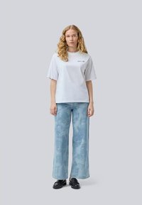 Short-sleeve white t-shirt with logo on the chest, paired with light blue wide-leg pants featuring a subtle cloud-like pattern and black shoes.