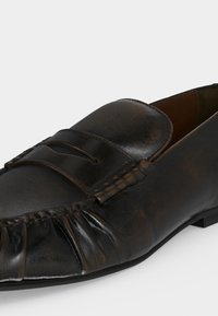 Μαύρη δερμάτινη μοκασίνη με ραφές μοκασίνου και λουράκι τύπου penny πάνω από το άνω μέρος σε λευκό φόντο.