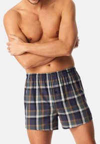 Boxer a quadri in blu navy, marrone e bianco con elastico in vita e bottone. Realizzati in tessuto leggero con una vestibilità rilassata.