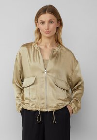 Goldfarbene Satin-Bomberjacke mit einem Reißverschluss, elastischen Bündchen, zwei Fronttaschen und einem Kordelzugsaum. Weiche Textur und lässige Passform.