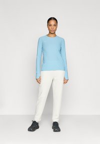 Top lung cu mâneci lungi de culoare albastră deschisă, cu guler rotund, asortat cu pantaloni albi și încălțăminte sport negre. Material neted și design ajustat.