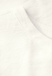 T-shirt bianca in cotone con una texture morbida, caratterizzata da un collo rotondo e un sottile dettaglio di cucitura lungo il colletto.