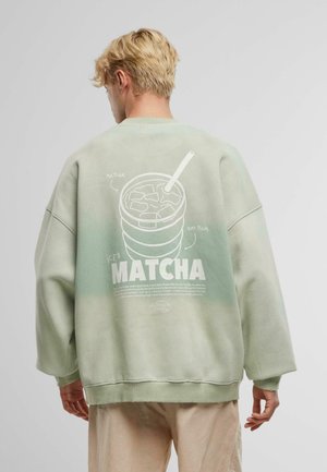 Oversized green sweatshirt, featuring a white graphic print of a drink cup with straw on the back, soft cotton material, ribbed hem.