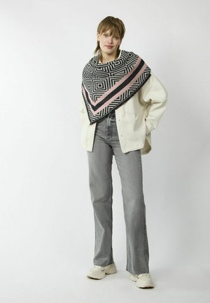 Foulard à motif géométrique noir et blanc avec des accents roses, porté sur une chemise oversized crème clair et un jean gris, associé à des baskets blanches.