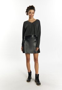 Schwarzer, kurzer Pullover mit strukturiertem Strickmuster, kombiniert mit einem schwarzen A-Linien-Rock aus Leder und schwarzen Schnürkampfstiefeln.
