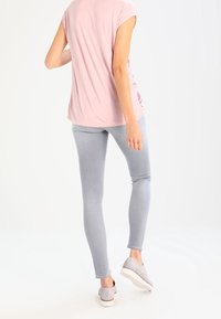 Haut rose clair à manches courtes avec une coupe décontractée, associé à un jeans gris clair ajusté et des chaussures à enfiler grises, vu de dos.