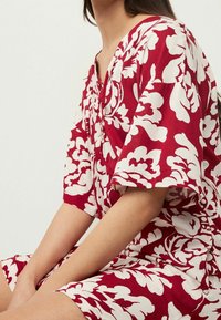 Robe ample à motif floral rouge et blanc en tissu léger, dotée de manches courtes et d'un décolleté en V.