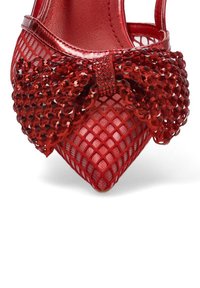 Zapato de tacón alto rojo con detalles de malla, un elegante lazo texturizado y diseño de puntera puntiaguda. El zapato tiene una superficie brillante y acentos decorativos.