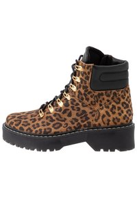 Stivale alla caviglia con stampa leopardata, corpo in suede color sabbia, rifiniture in pelle nera, occhielli dorati e una suola nera spessa con una finitura testurizzata.