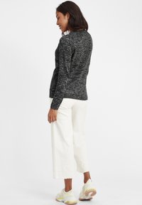 Pull en tricot marbré noir et blanc, à manches longues, col rond, associé à un pantalon blanc court et des baskets légères avec des touches de couleur.